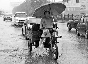 昨天，在王四營橋附近，一位騎三輪車的大爺打著傘在雨中前行。晨報記者 王巍/攝